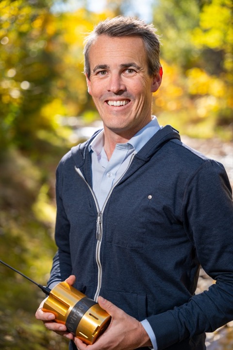 Evan Thomas outdoors in autumn, holding a gold Lume water quality sensor
